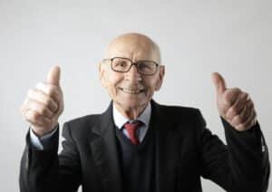 Cheerful elderly man in suit giving thumbs up, symbolizing success and approval.